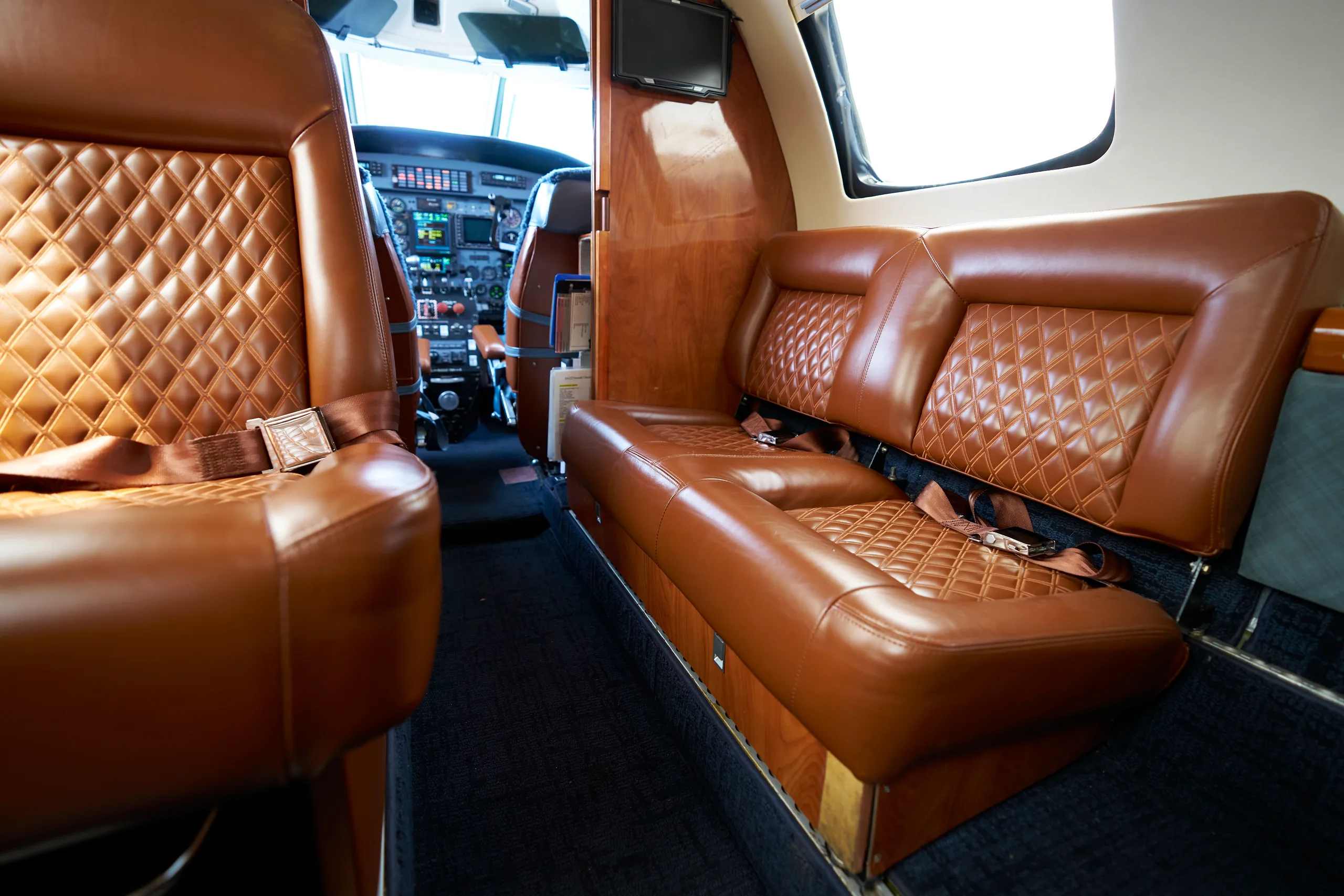 A view inside the aircraft cabin showing brown quilted leather seats and the cockpit in the distance.