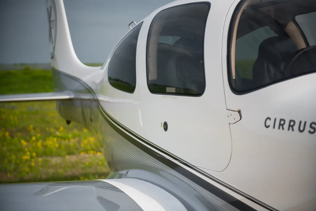 A close-up view of the side of a white and silver Cirrus SR22T aircraft, showing the cabin windows and part of the wing.