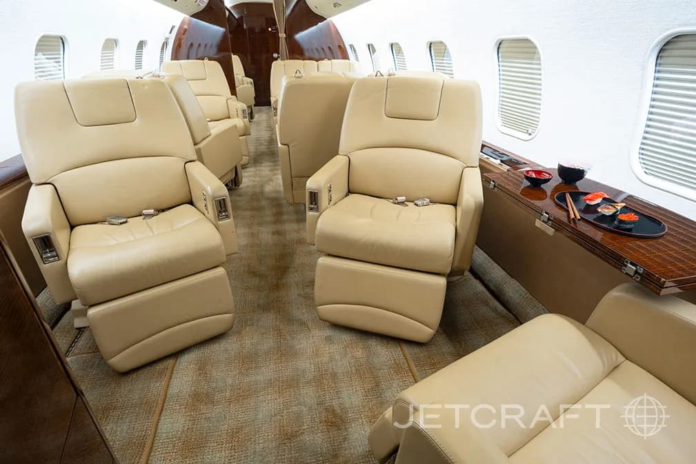 A private jet cabin interior featuring beige leather seats, a side table with sushi, and a patterned carpet.