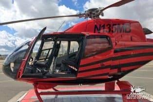 A red and black helicopter with the tail number N135MB with the door open.