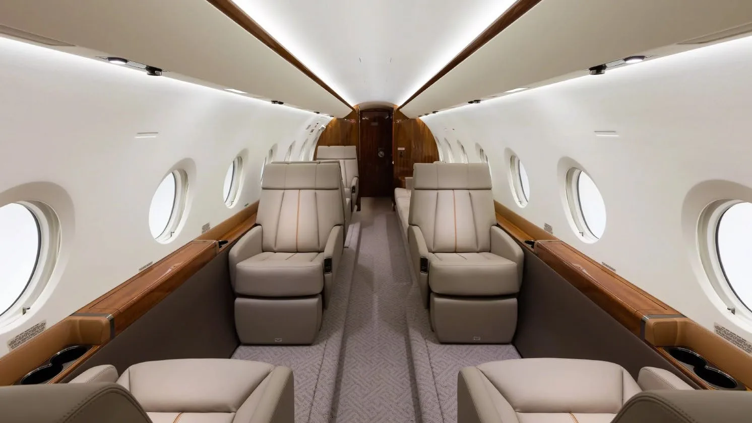 A view down the aisle of a luxurious aircraft cabin with beige leather seats and wood trim.