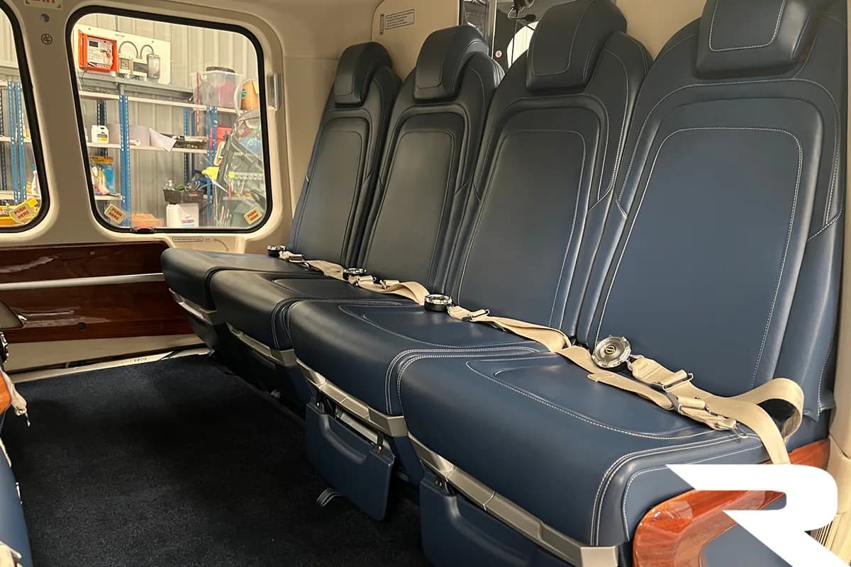 Interior view of a helicopter cabin with a row of blue leather seats, looking towards the front.