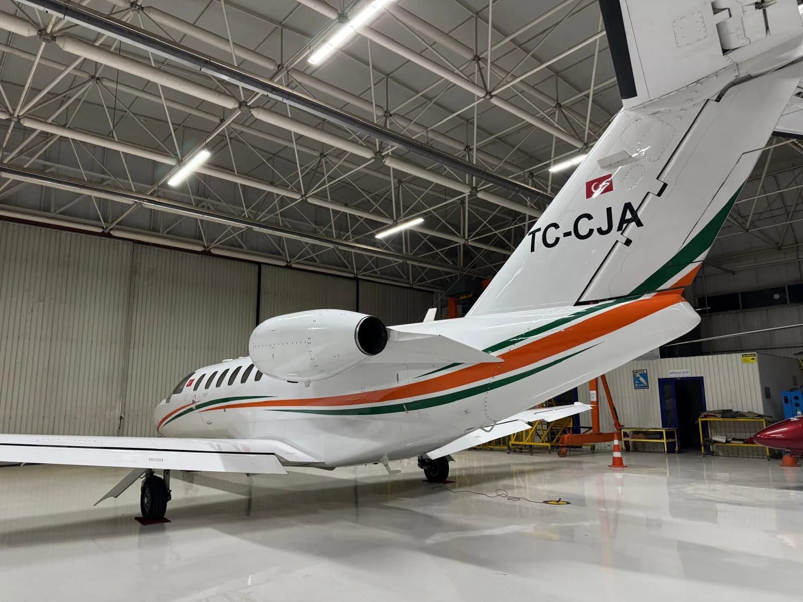 Rear view of a white business jet with orange and green stripes and Turkish flag tail number TC-CJA, parked in a hangar.