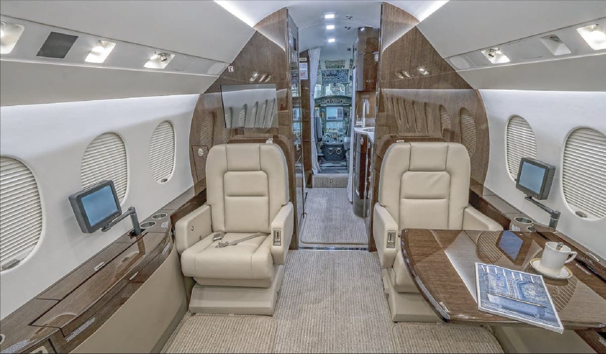 View of the interior cabin of a jet with leather seats and wood trim.