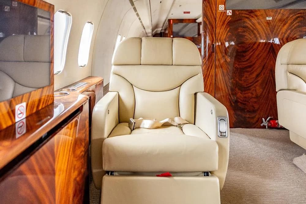 A single cream leather seat with a footrest in a luxurious aircraft cabin.