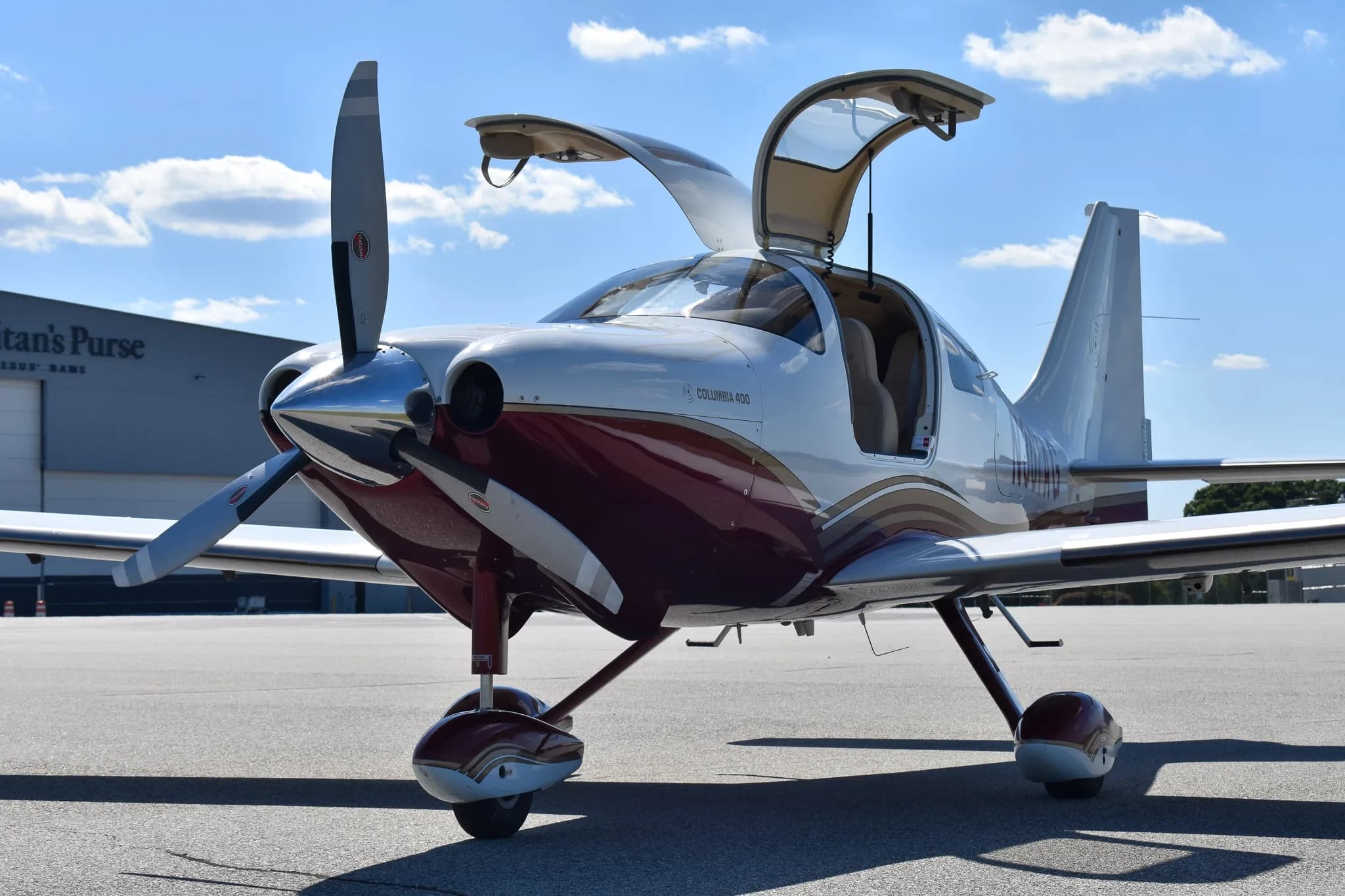 Front view of a white and maroon Columbia 400 aircraft with its doors open on an airfield.