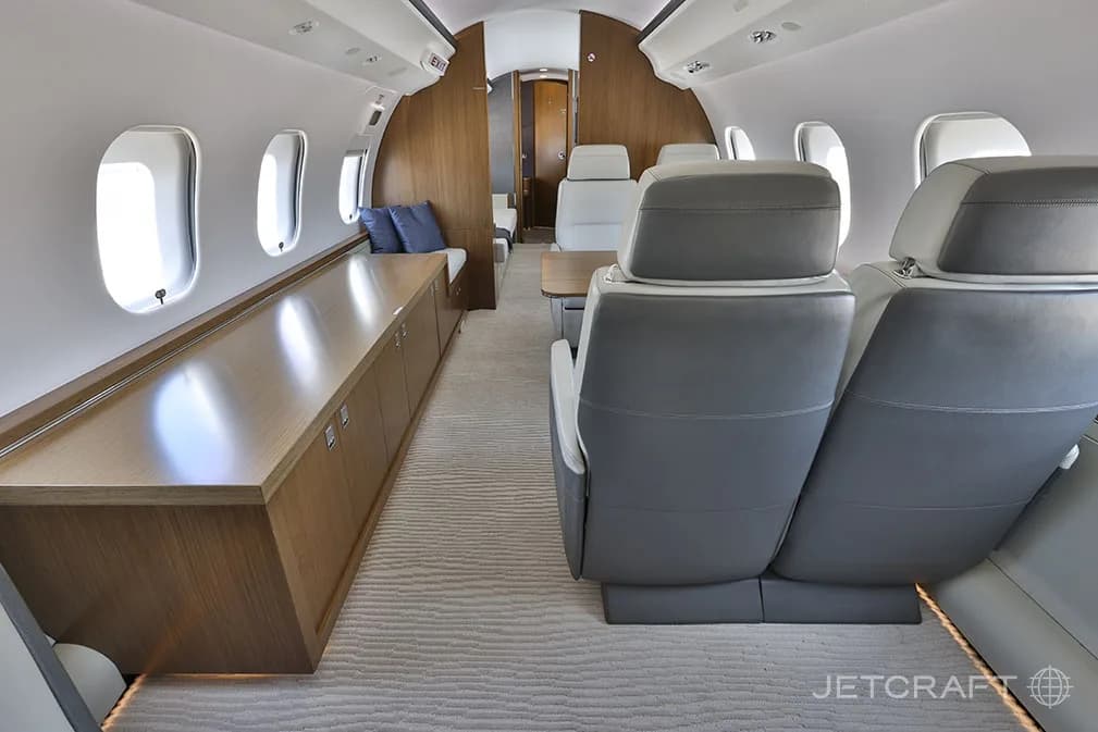 The rear section of the Bombardier Global 6000 cabin, with a long wooden credenza on one side and grey leather seats facing forward.