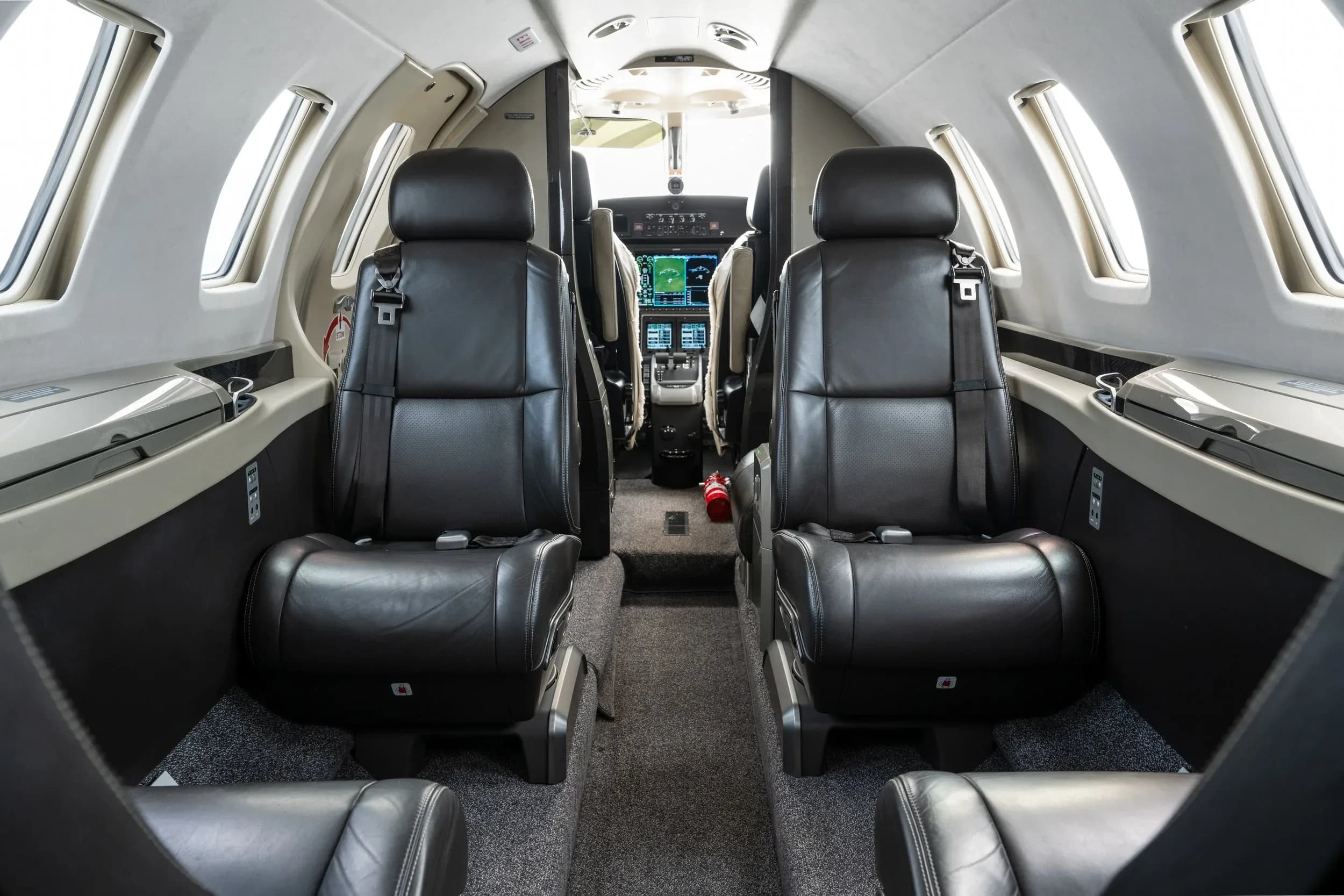 View of the aircraft cabin with two black leather seats in the foreground and the cockpit visible in the distance.