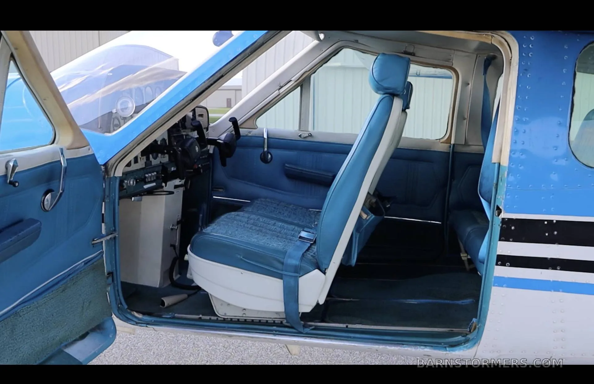 The blue interior of a Cessna 210 Centurion, showing the front passenger seat and part of the cockpit with the door open.