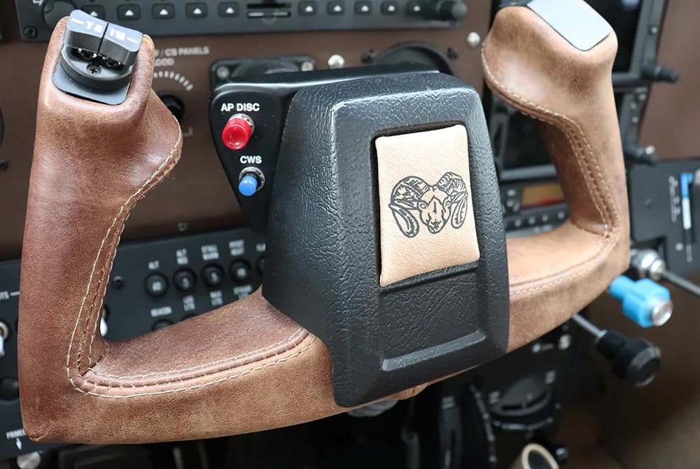 A close-up of an aircraft's brown leather-wrapped yoke with a ram's head logo embossed on it.