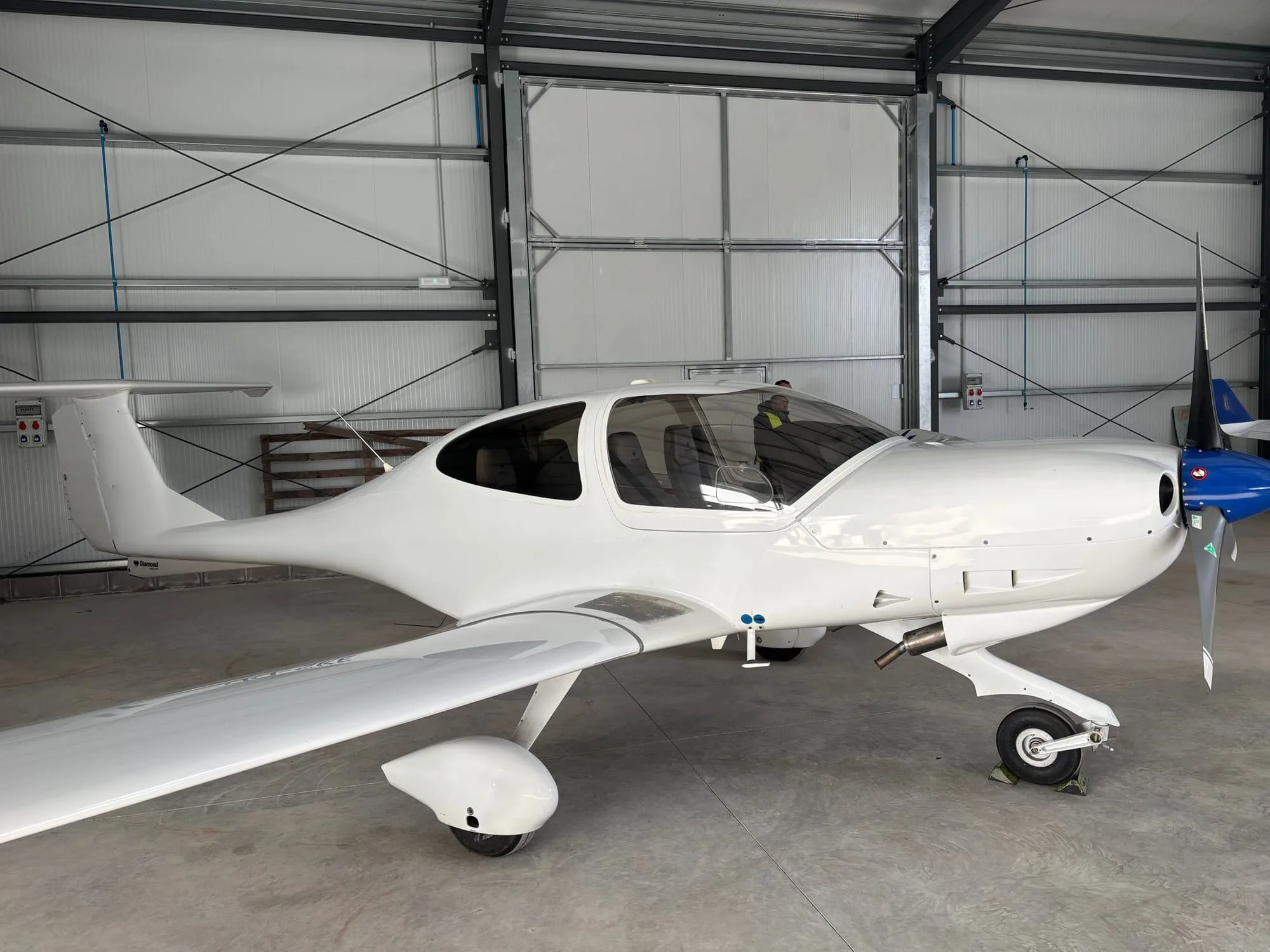 A white Diamond DA40 aircraft is parked inside a hangar.