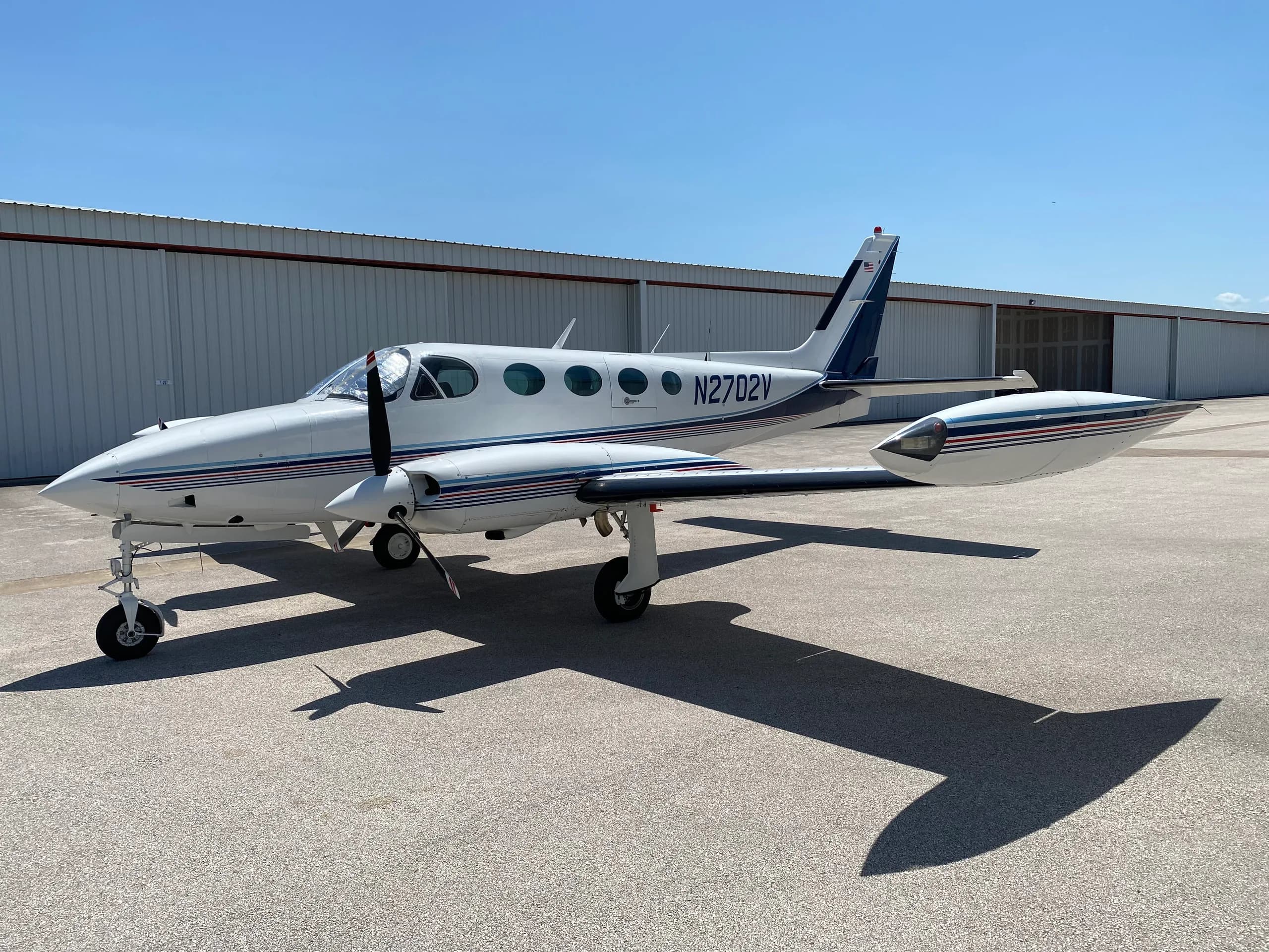 A Cessna 340A aircraft with registration N2702V parked in front of a hangar.