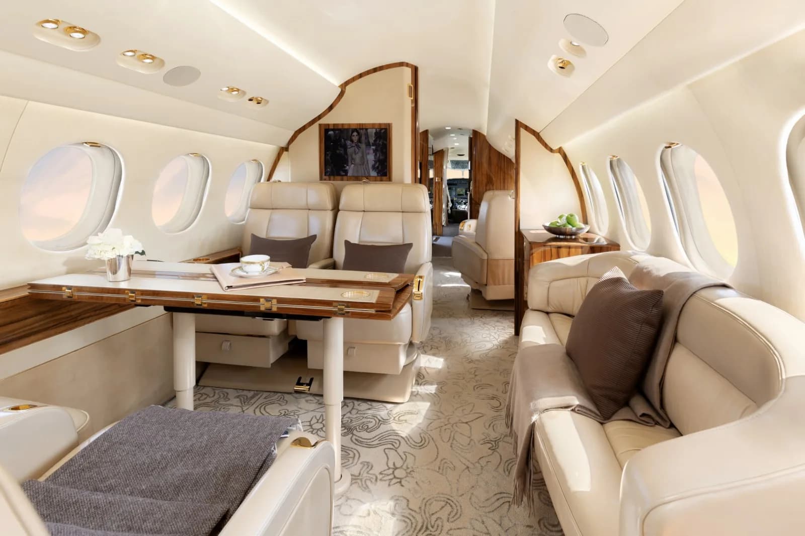 Interior of the aircraft with leather seats, a sofa, and a wooden table with a tea set.