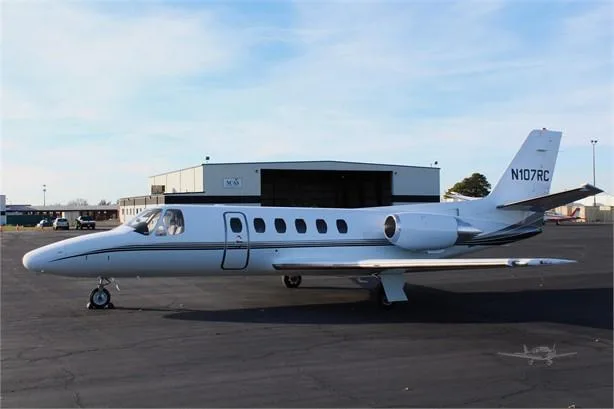 A white Cessna Citation jet, registration N107RC, is parked on an asphalt tarmac with hangars in the background.