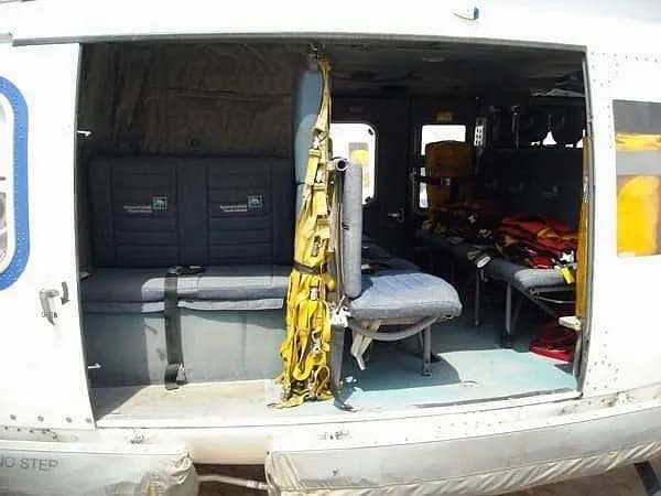 The interior of a helicopter cabin showing grey bench seats, a yellow harness, and red life vests.