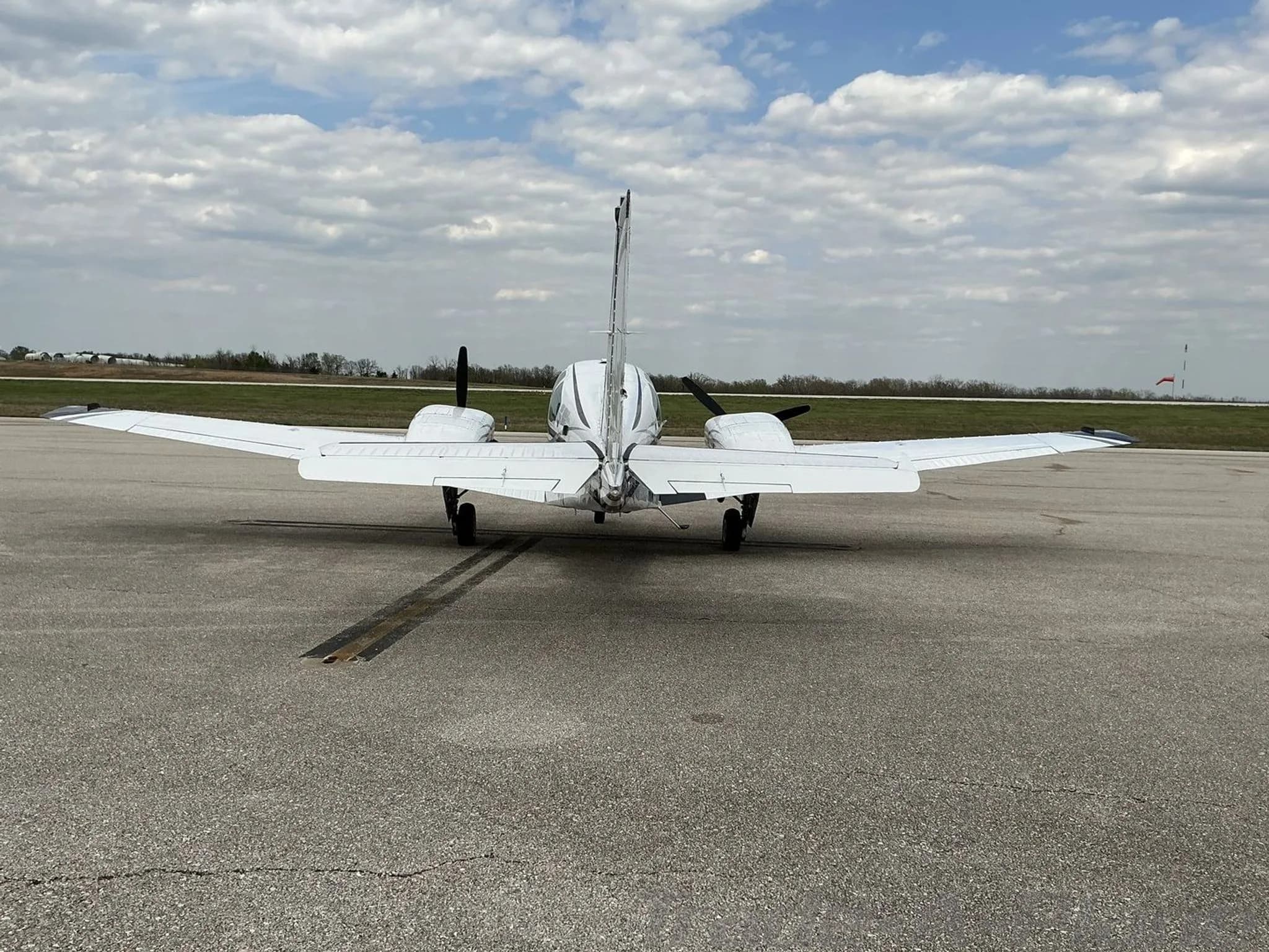 A rear view of a white twin-engine propeller aircraft with black and maroon stripes parked on an asphalt tarmac.