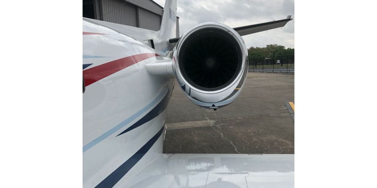 A close-up view of the jet engine and rear fuselage of a white Cessna Citation with red and blue stripes, parked outdoors.