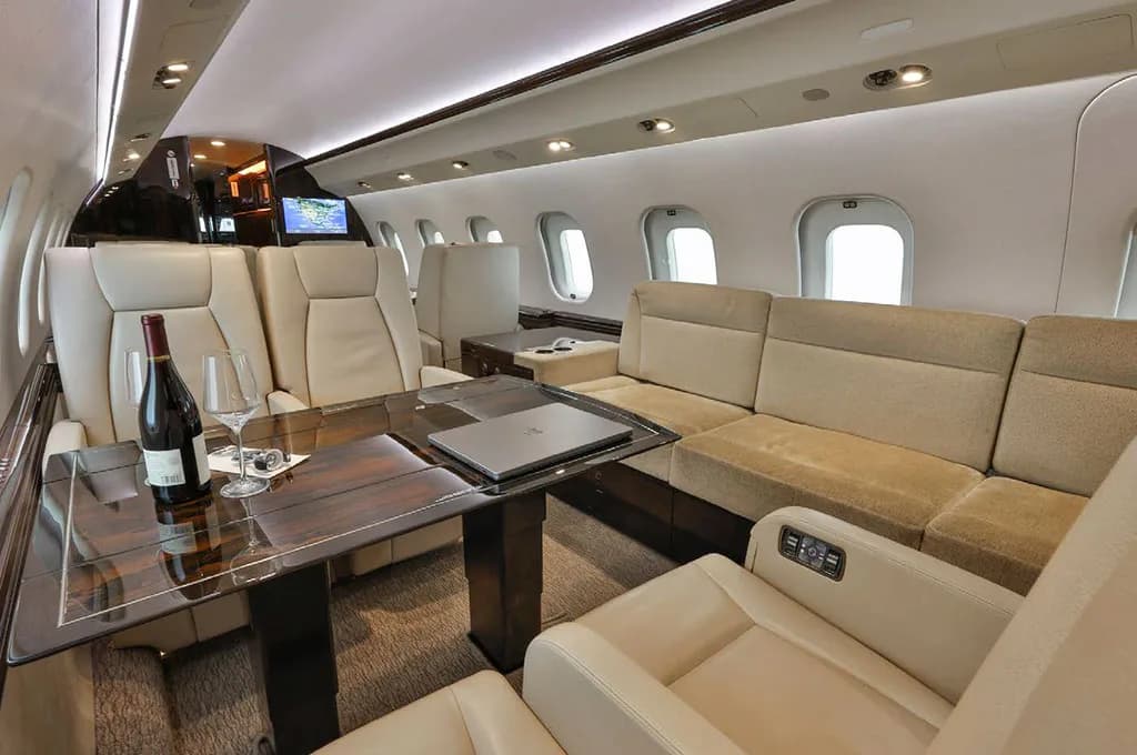 The spacious cabin interior of a business jet, featuring a beige sofa, individual seats, and a large table.