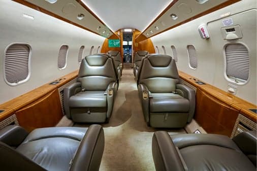 The luxurious interior of a business jet cabin with grey leather seats and wood paneling.