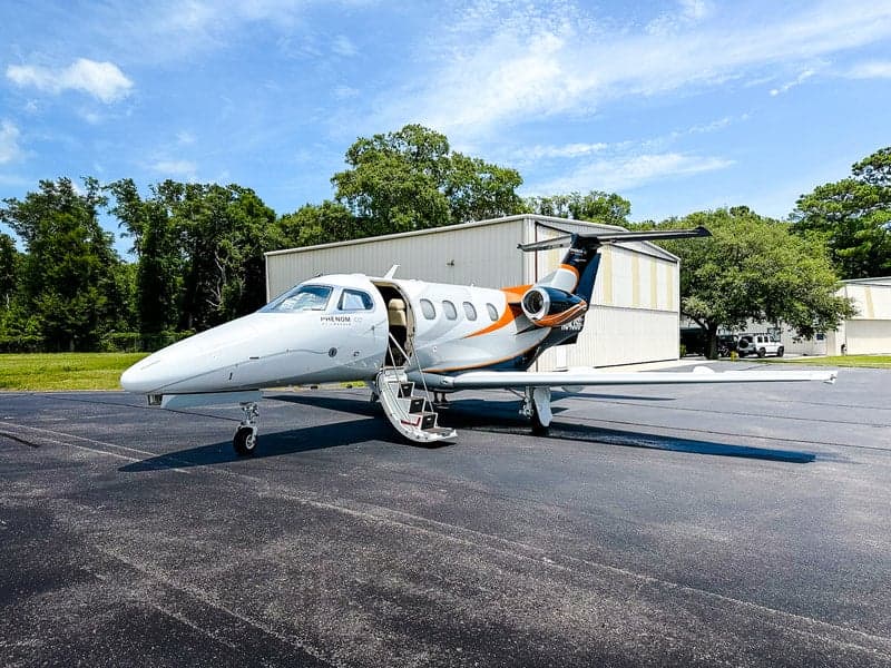 A Phenom 100 aircraft with an open door is parked on the tarmac.