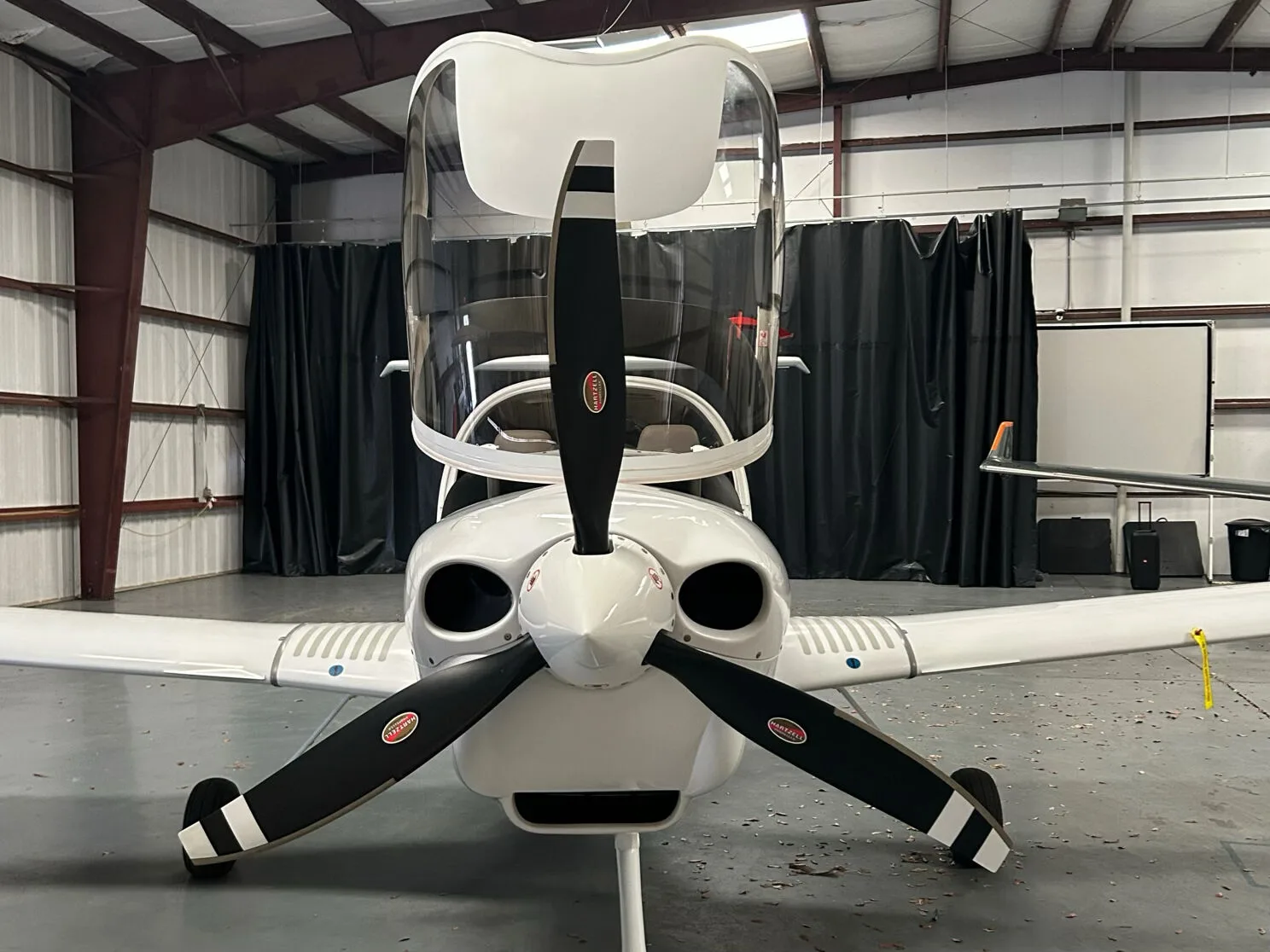 Front view of a white Diamond DA40 aircraft with its canopy open, parked in a hangar.