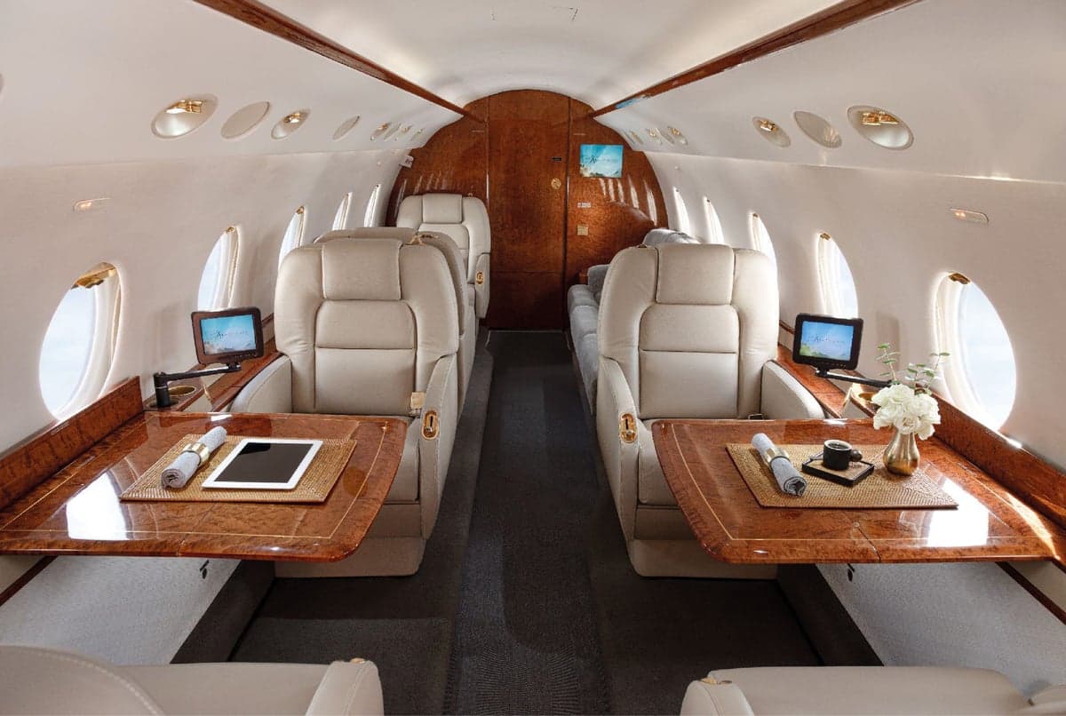 Aircraft cabin featuring leather seats and tables.
