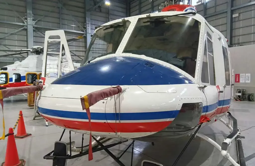 Front view of a white helicopter with a blue nose and red and blue stripes, parked in a hangar.