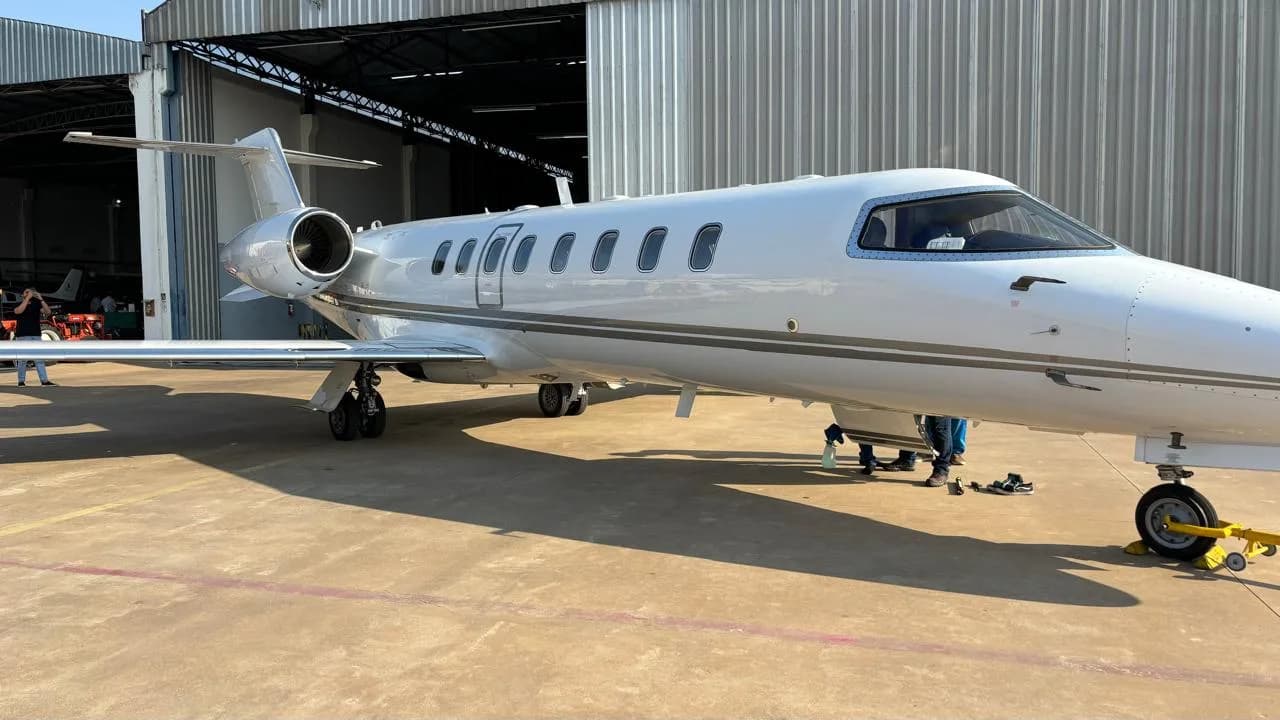 A white business jet with engines on the fuselage parked outside a hangar.
