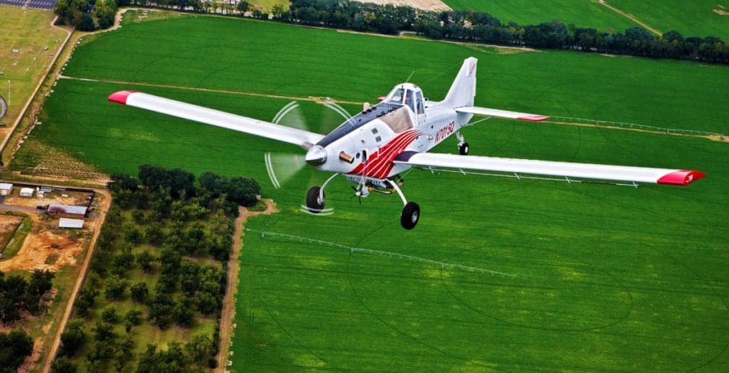 Aerial view of an Air Tractor 710P agricultural aircraft in flight over a field.