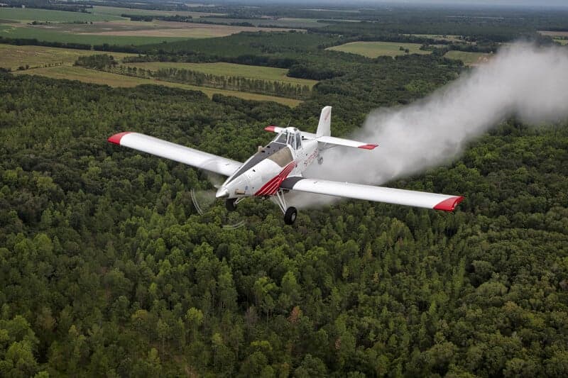 A Thrush aircraft spraying crops over a forest.
