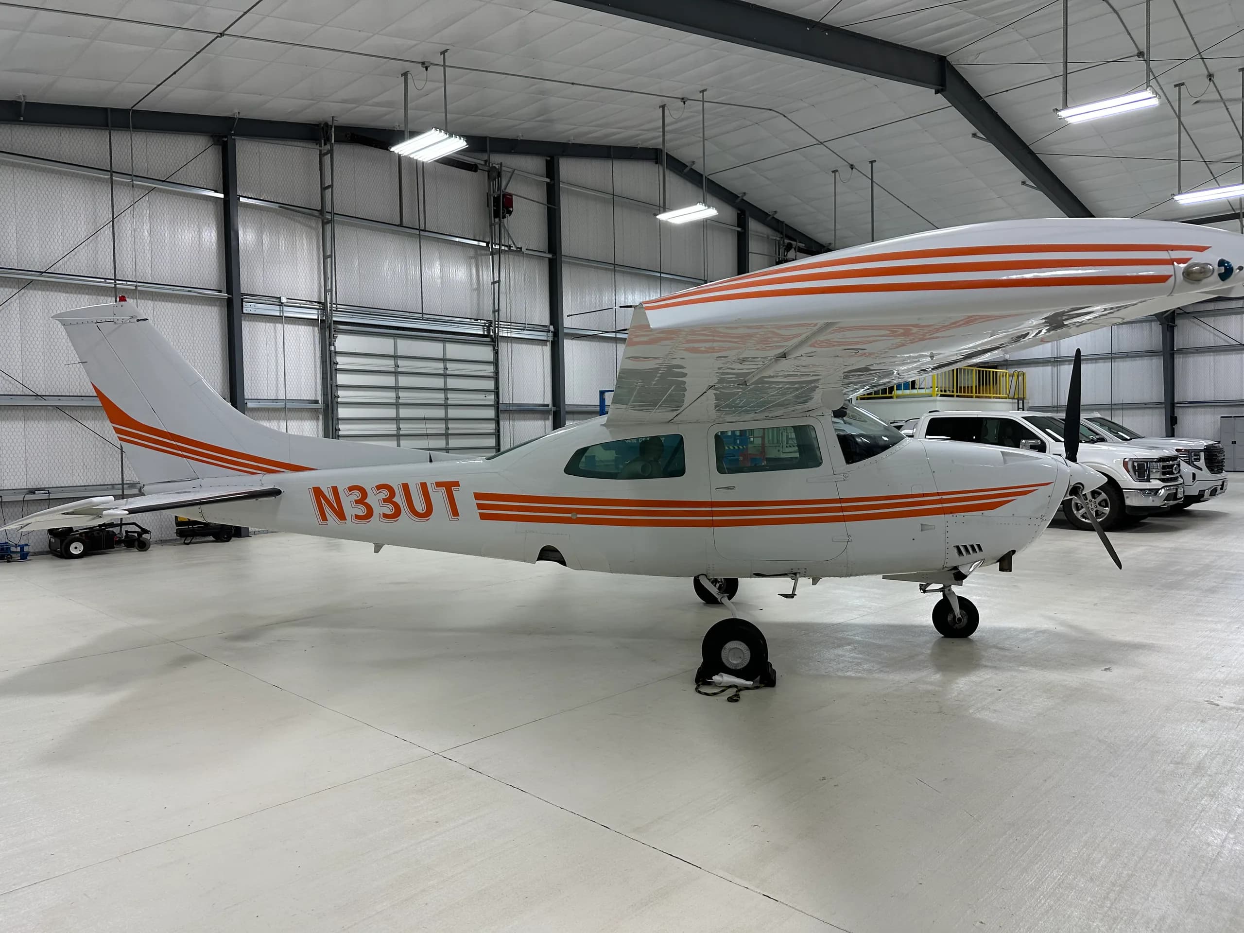 A Cessna 206 Stationair aircraft with orange stripes parked in a hangar.