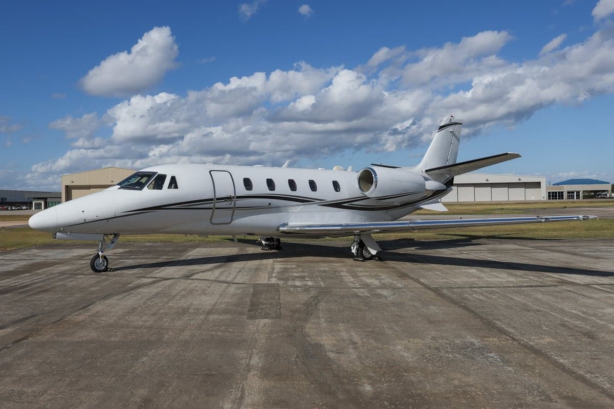 A Citation CJ3 aircraft is parked on the tarmac in front of hangars.