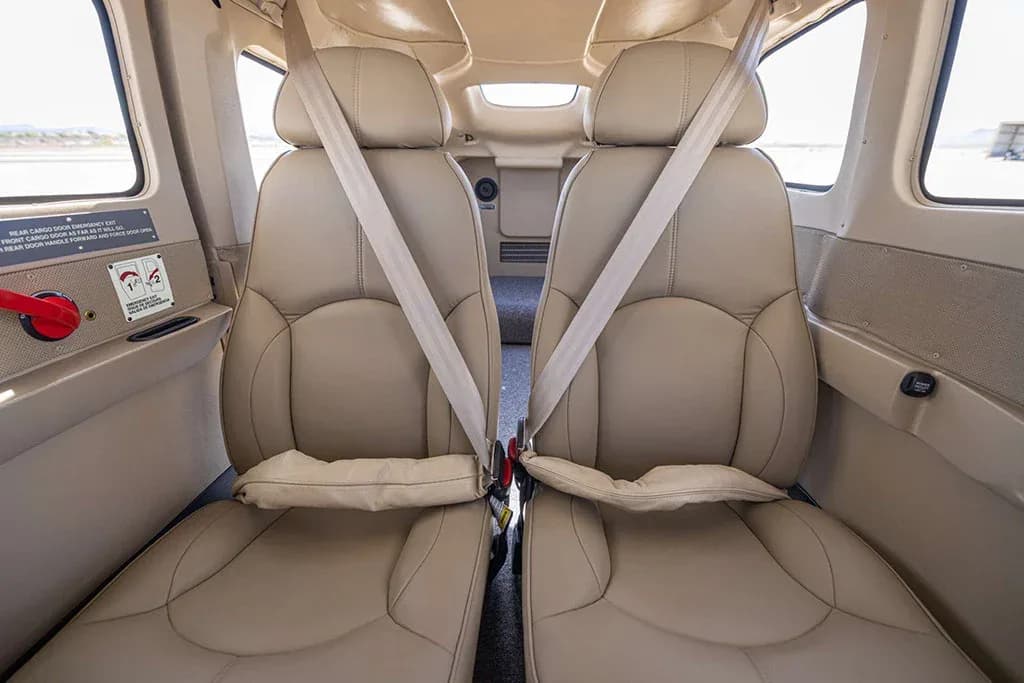 Two tan leather rear passenger seats with seatbelts in the aircraft cabin.