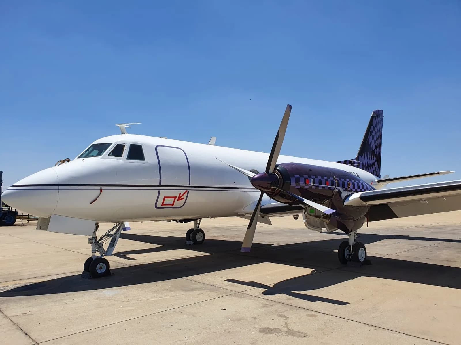 A white turboprop aircraft with a purple tail design parked on the tarmac under a clear sky.