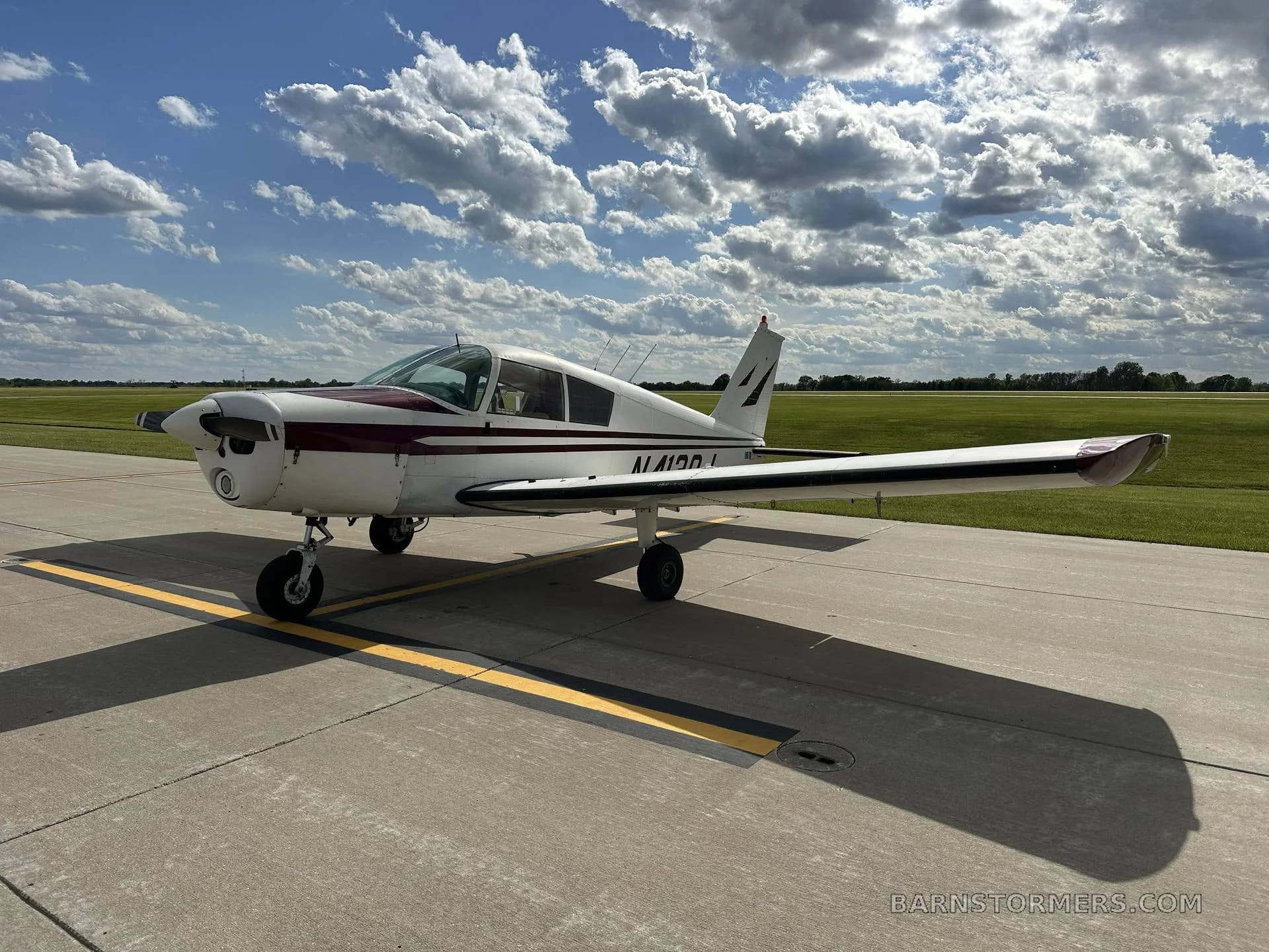 A white and maroon single-engine propeller aircraft, registration N4120J, is parked on an asphalt ramp under a partly cloudy sky, viewed from the front-left.