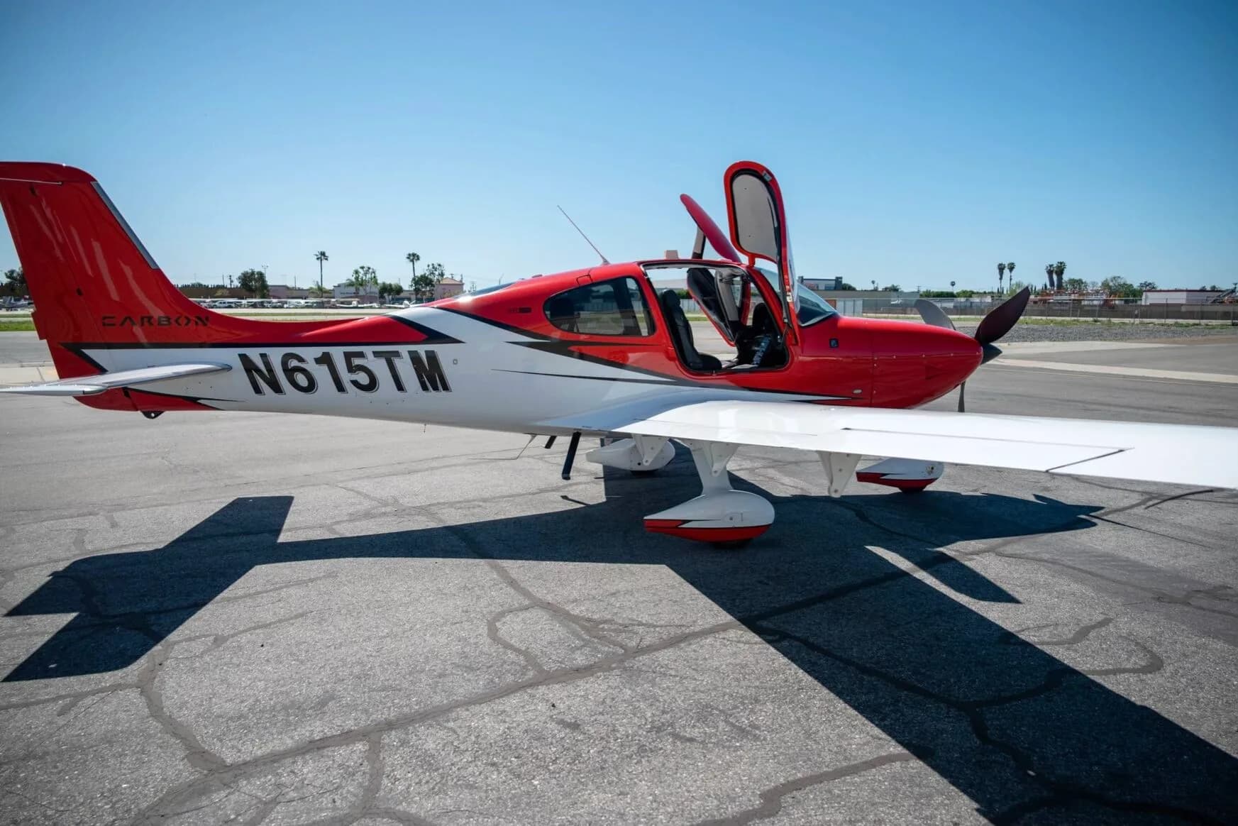 Side view of a red and white N615TM aircraft with its door open on an airfield.
