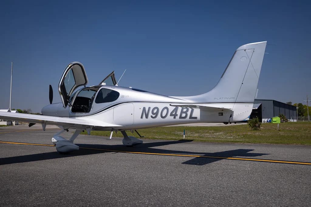 A side view of the silver Cirrus SR22 aircraft N904BL with its doors open, parked on an airfield.