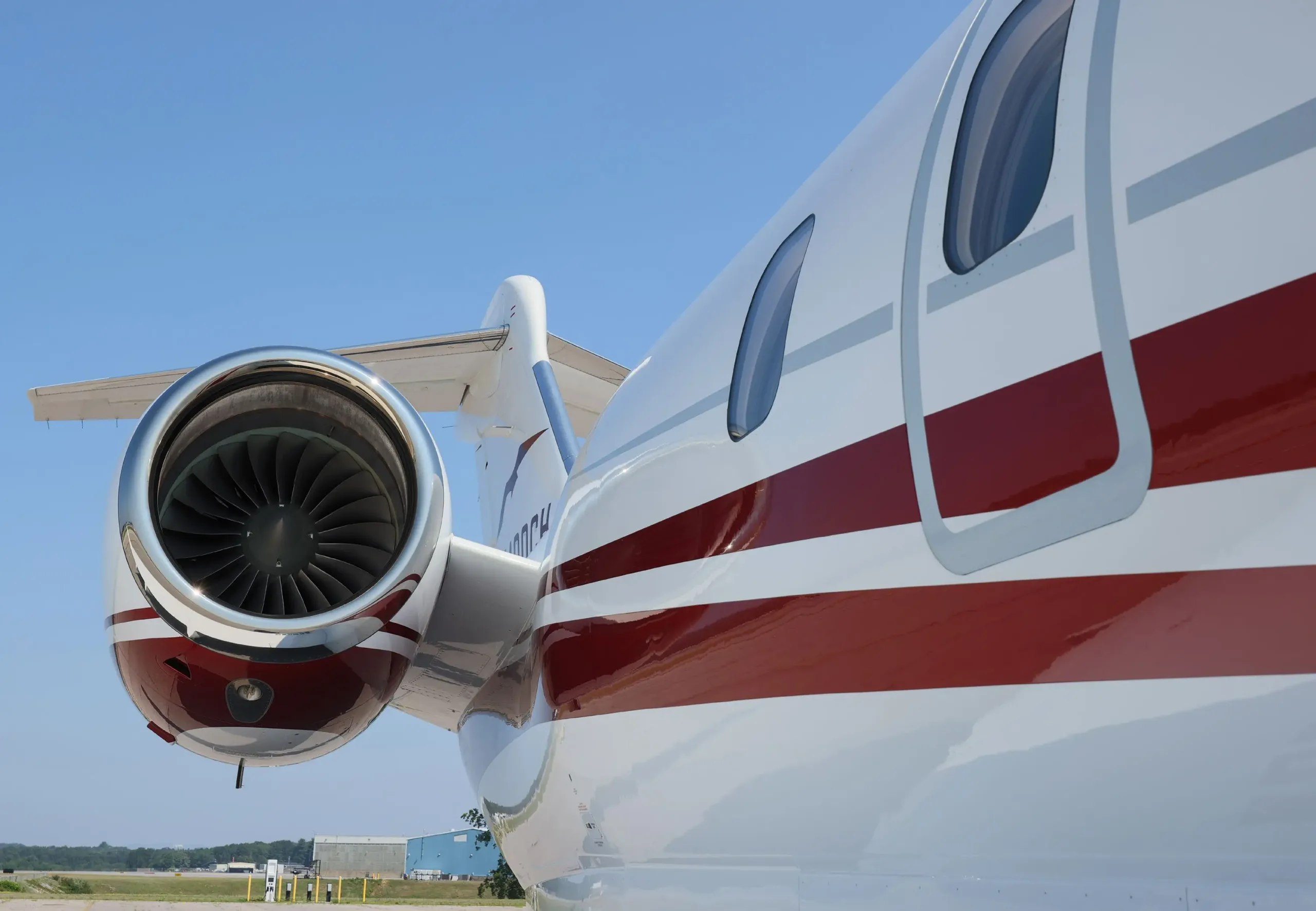 Close-up view of the rear engine and fuselage of a white business jet with red and grey stripes, showing registration N111EL.