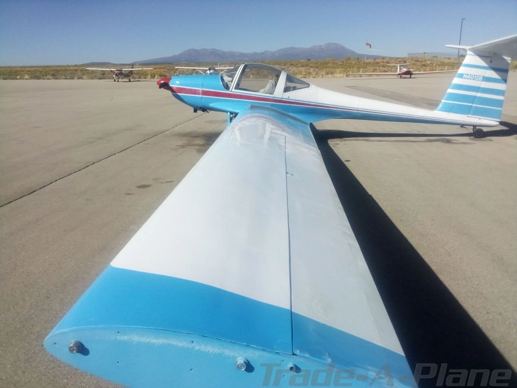 A blue and white aircraft with a red stripe, tail number N4012B, parked on an airfield with mountains in the background.