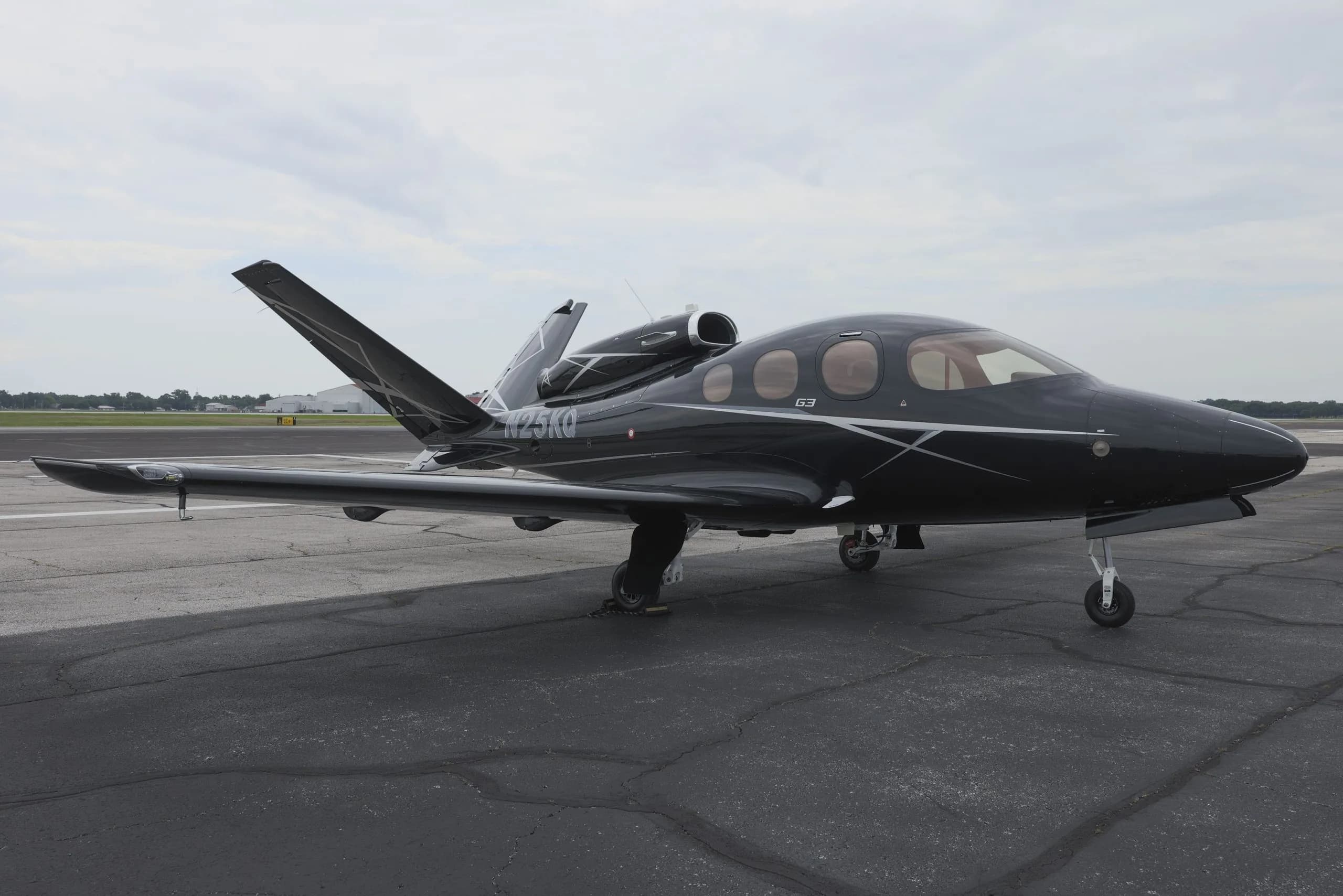 A black Cirrus Vision Jet (N25KQ) with white and grey accents is parked on a tarmac, viewed from the front-right.