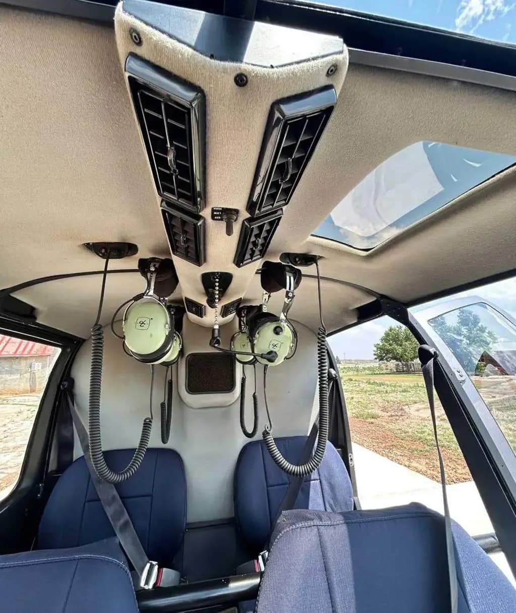 The interior cabin of a Robinson R44 helicopter showing blue seats, overhead vents, and headsets.