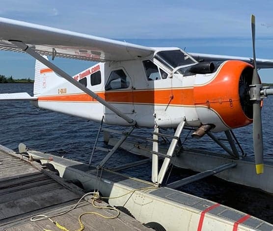 A de Havilland Beaver floatplane is docked on a wooden platform on a lake.