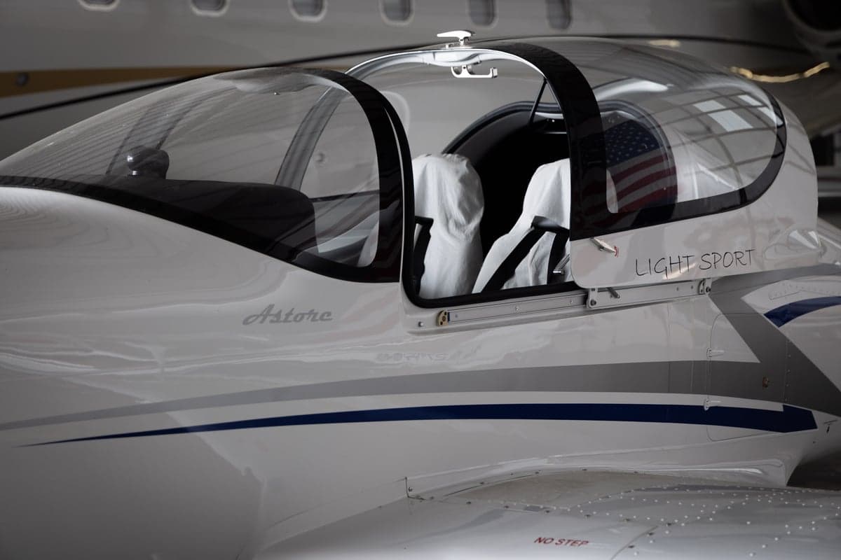 A close-up of the clear canopy and white fuselage of a Tecnam Astore light sport aircraft, showing the "Astore" and "Light Sport" text.