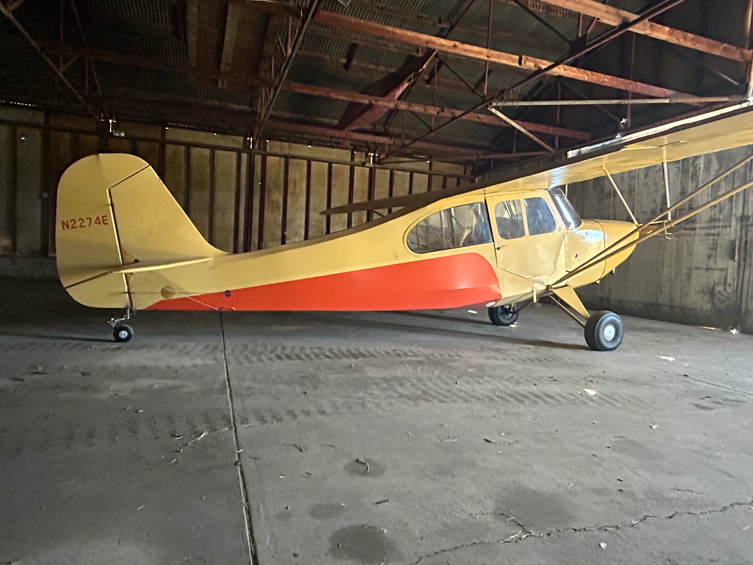 A yellow and orange Aeronca 7AC Champ aircraft with tail number N2274E parked inside a hangar.