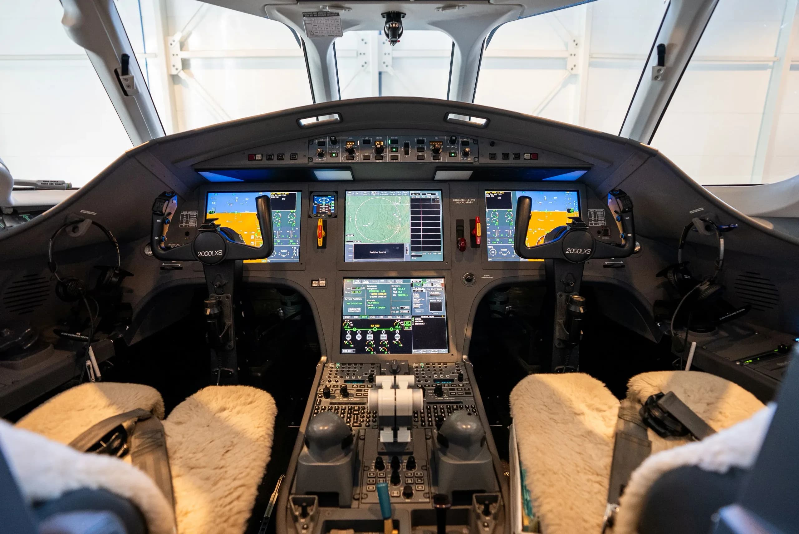 The modern cockpit of a private jet, featuring multiple digital displays, control yokes, and a central control panel.