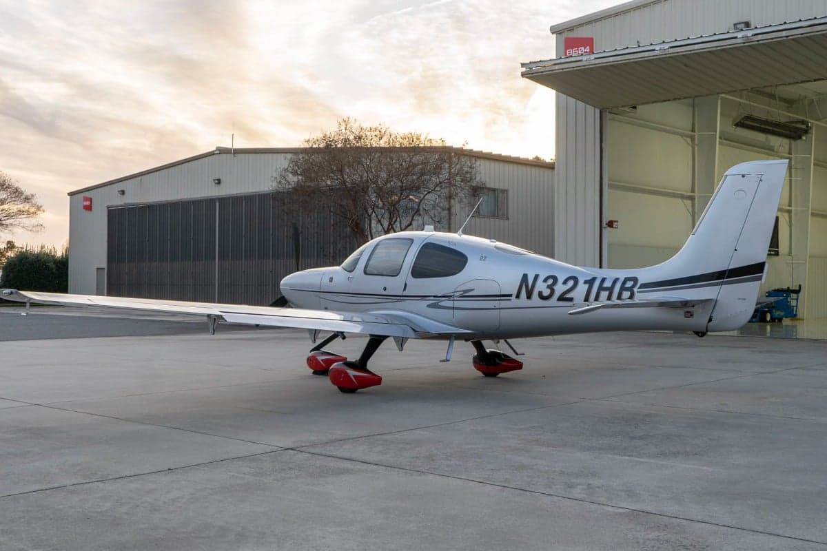 A Cirrus SR22T aircraft with a silver paint scheme parked outside a hangar.