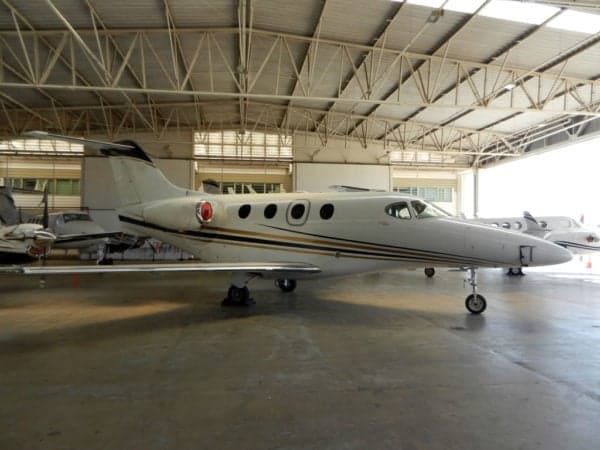 Side view of a white jet with gold stripes parked in a hangar.