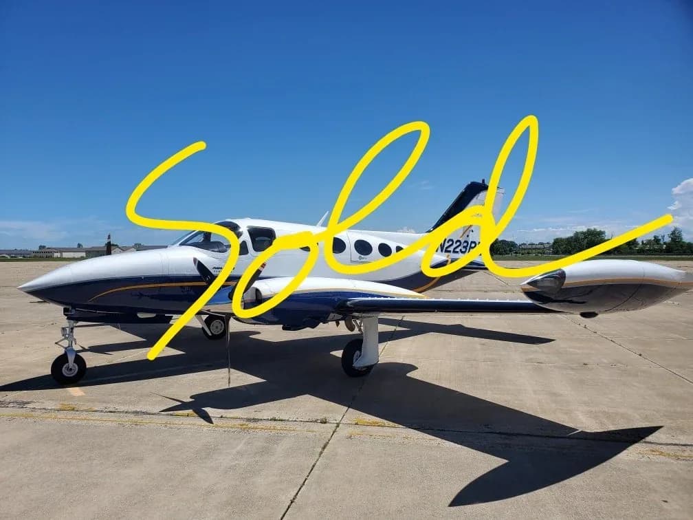 A white and blue twin-engine Cessna 340 aircraft (N223P) is parked on an asphalt tarmac under a clear blue sky.