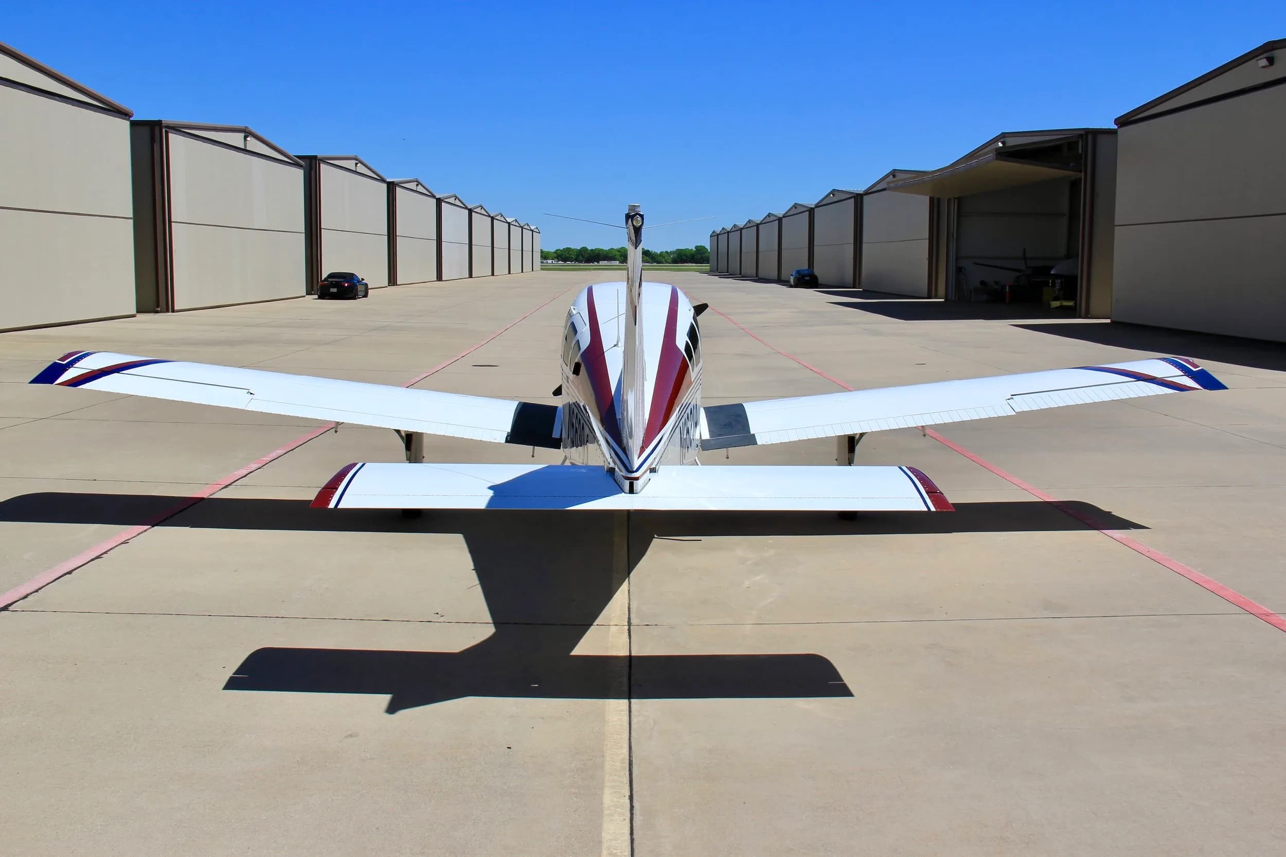 A rear view of the white, blue, and red single-engine aircraft (N66304) on an airport tarmac between hangars.