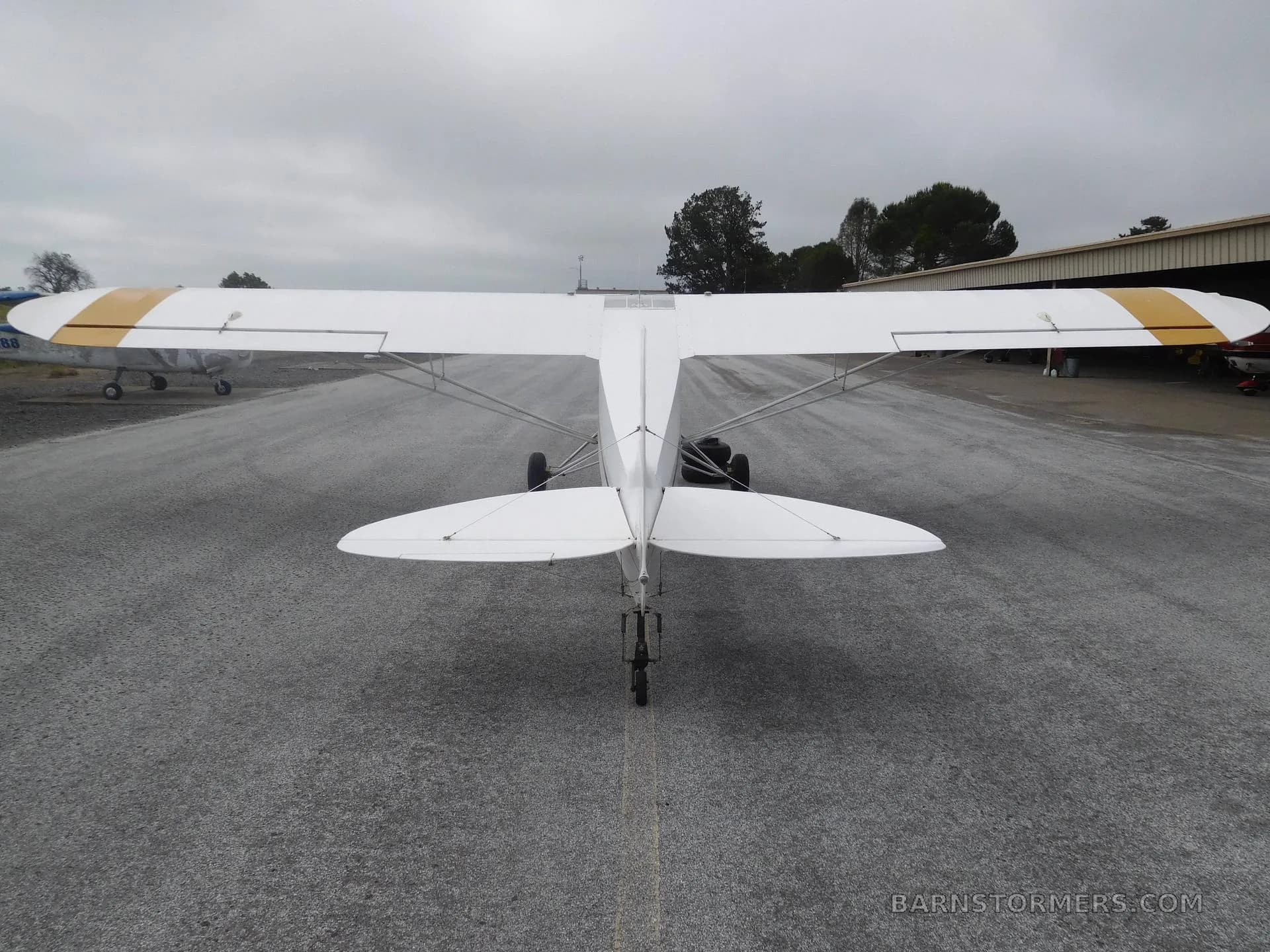 The rear view of a white experimental aircraft with gold wing stripes, parked on an asphalt runway.